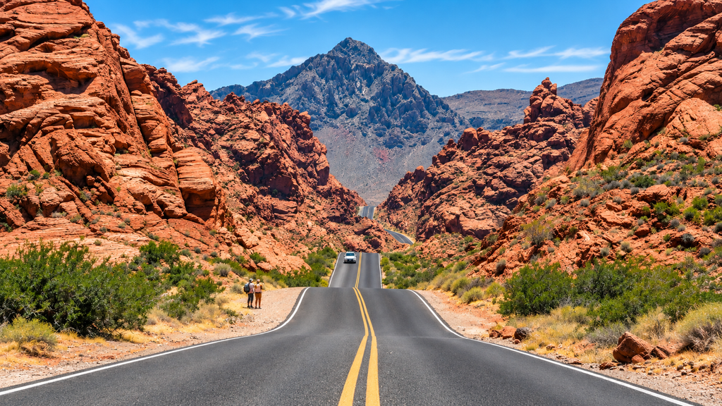 Scenic desert highway through red rock canyon with white car driving toward distant mountain, two hikers on roadside